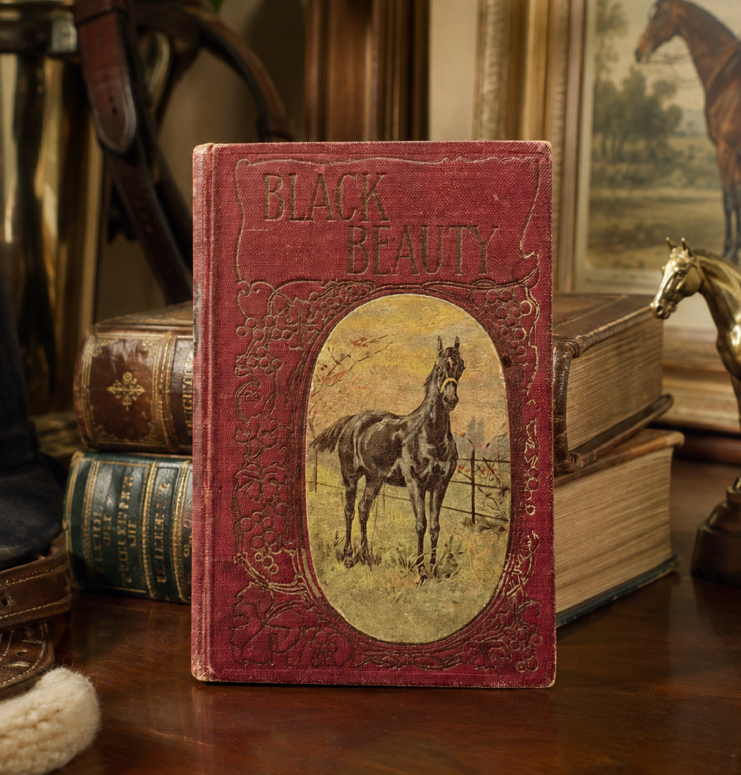 An antique red book titled 'Black Beauty' with an illustration of a horse on the cover, standing on a wooden table surrounded by old books and horse-themed decor.