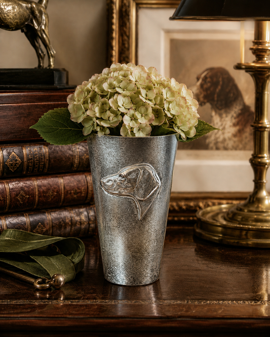 Decorative vase with a dog design on a wooden surface with books and a lamp in the background.