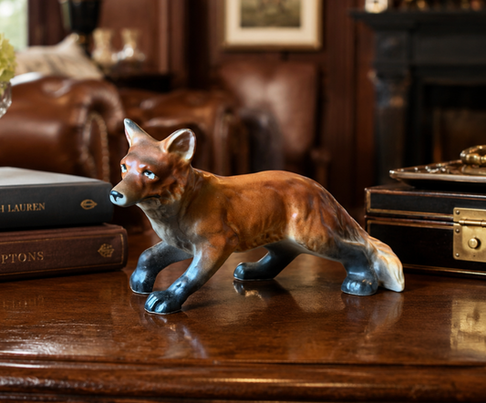 Fox figurine on a wooden surface with books and a suitcase in the background