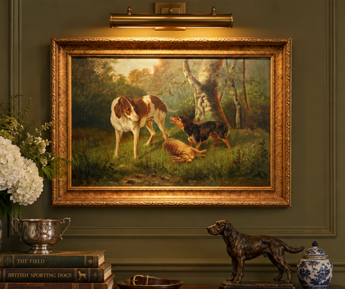 A framed vintage-style oil painting of two hunting dogs in a grassy woodland scene, displayed on a dark olive green wall above a console table with decorative objects including a dog statue, books, and a blue-and-white lidded jar.