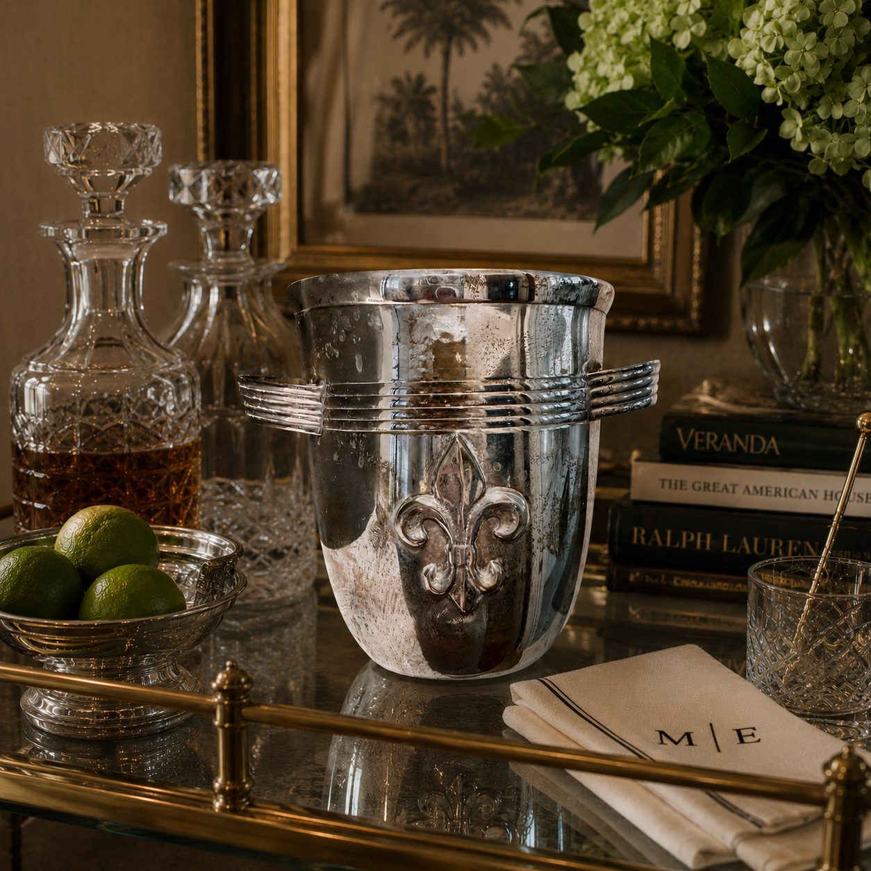 Silver ice bucket with fleur-de-lis design on a table with books and limes.