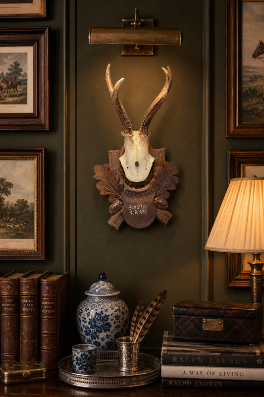 Decorative wall with mounted deer head, books, and lamp on a dark green wall.