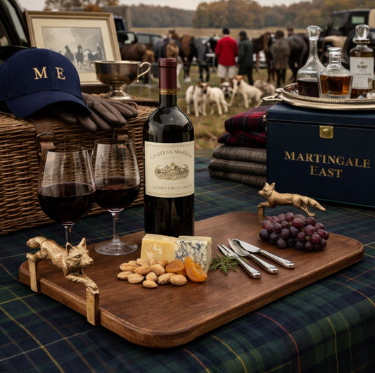 Wine bottle, glasses, and charcuterie board on a table with people and horses in the background.