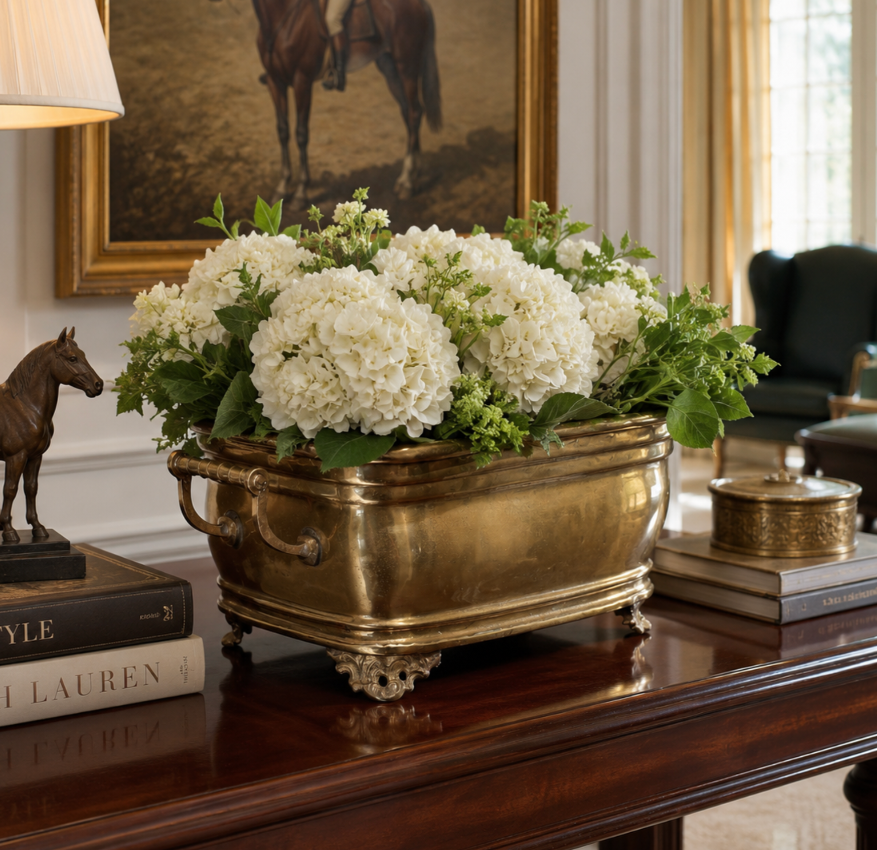 A large rectangular brass planter filled with white hydrangea blooms and green foliage, displayed on a polished dark wood console table in an elegant room setting.
