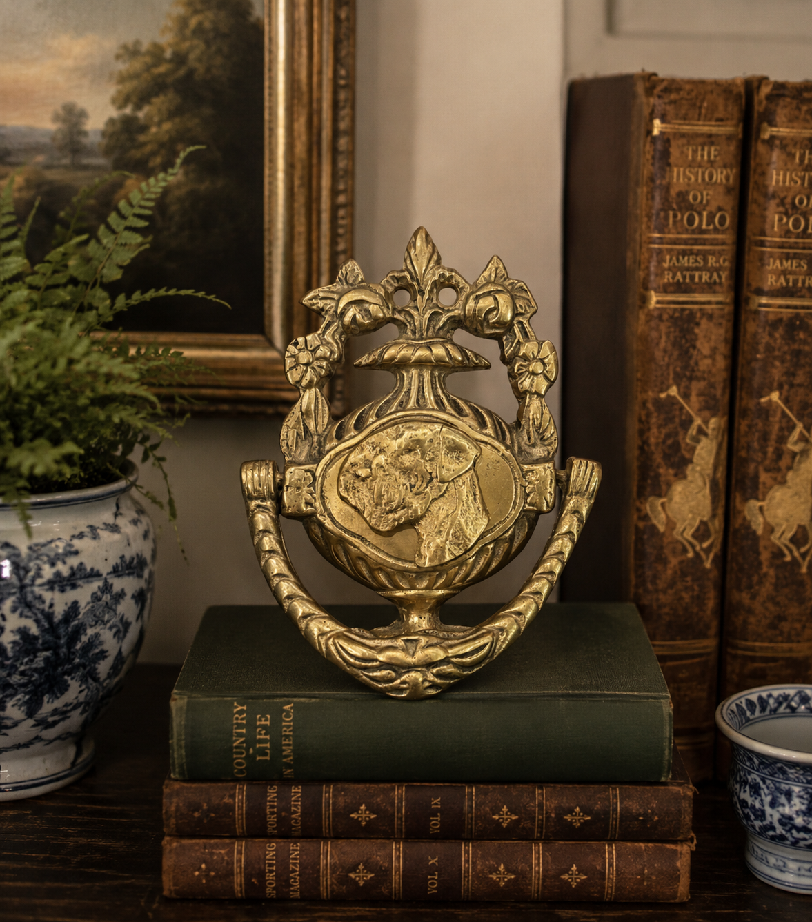 An ornate gold-toned decorative urn sculpture with a dog relief on the front, displayed on stacked vintage books in a styled interior setting.