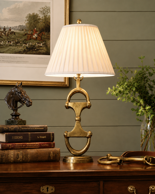 Decorative lamp with pleated shade on a wooden surface with books and a horse statue.