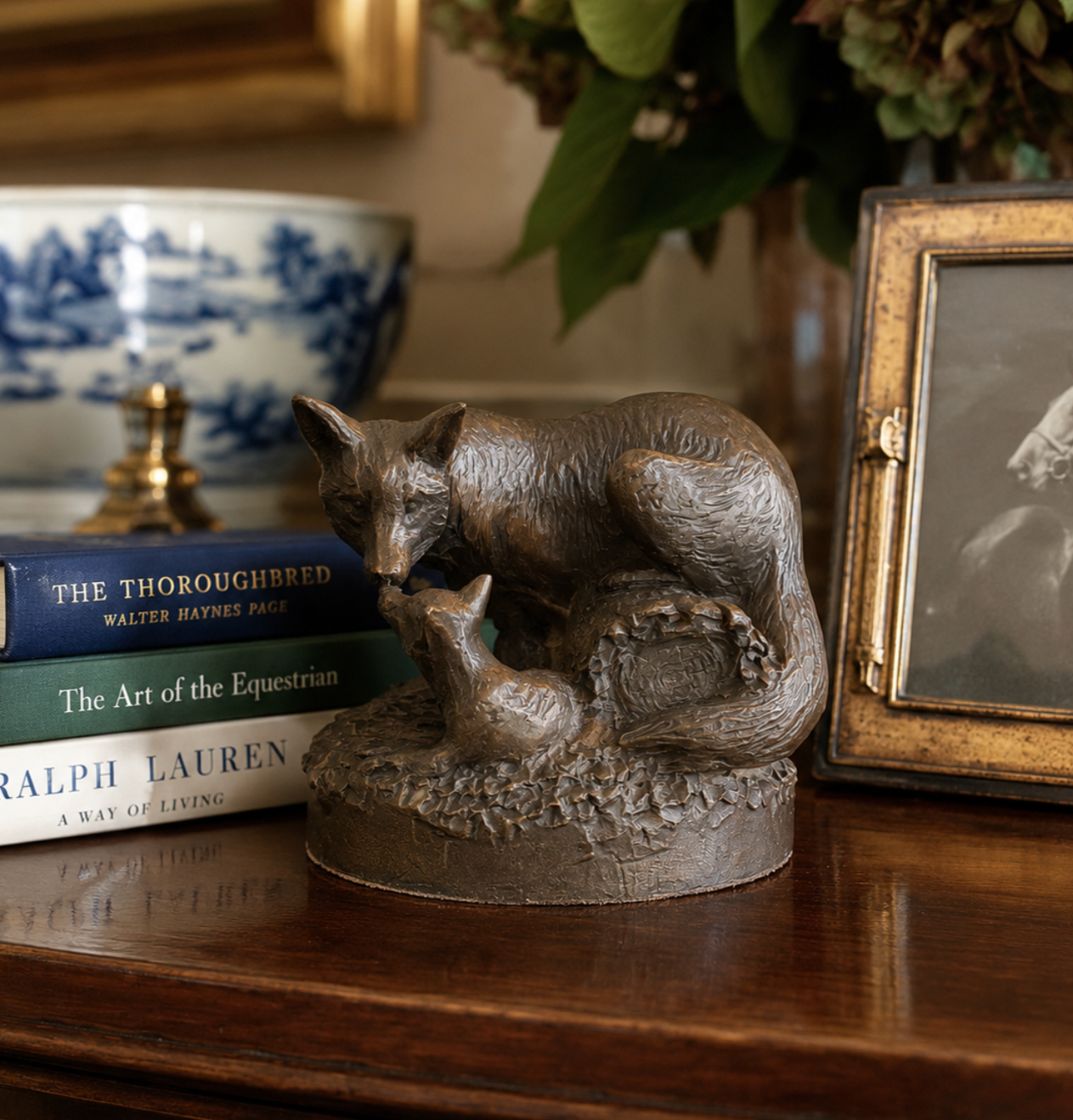 Bronze sculpture of two animals on a wooden surface with books and a photo frame in the background.