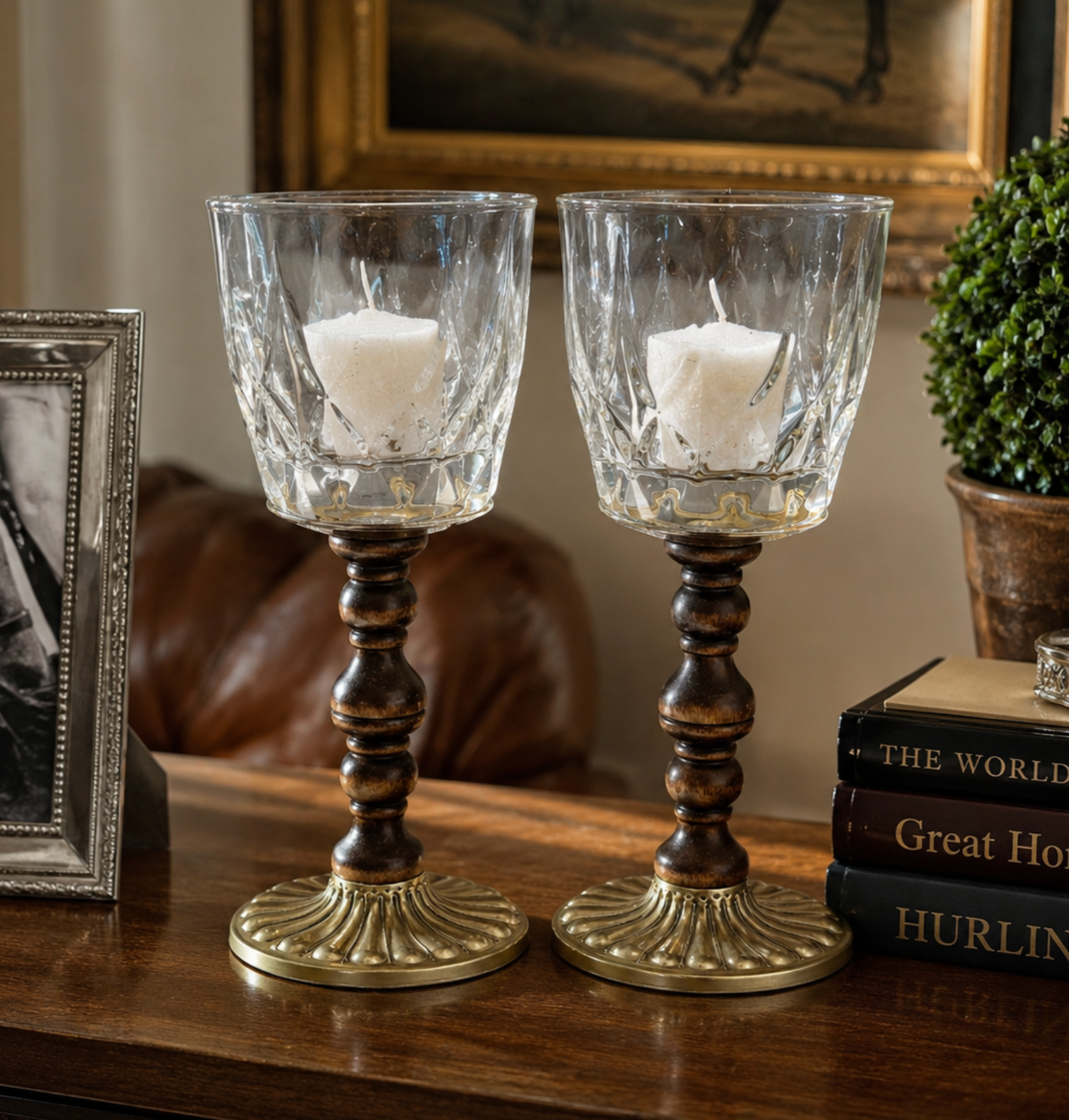 Two matching candle holders with clear textured glass cups, dark brown turned wood stems, and ornate gold-toned bases, displayed on a wooden table in a styled interior setting.