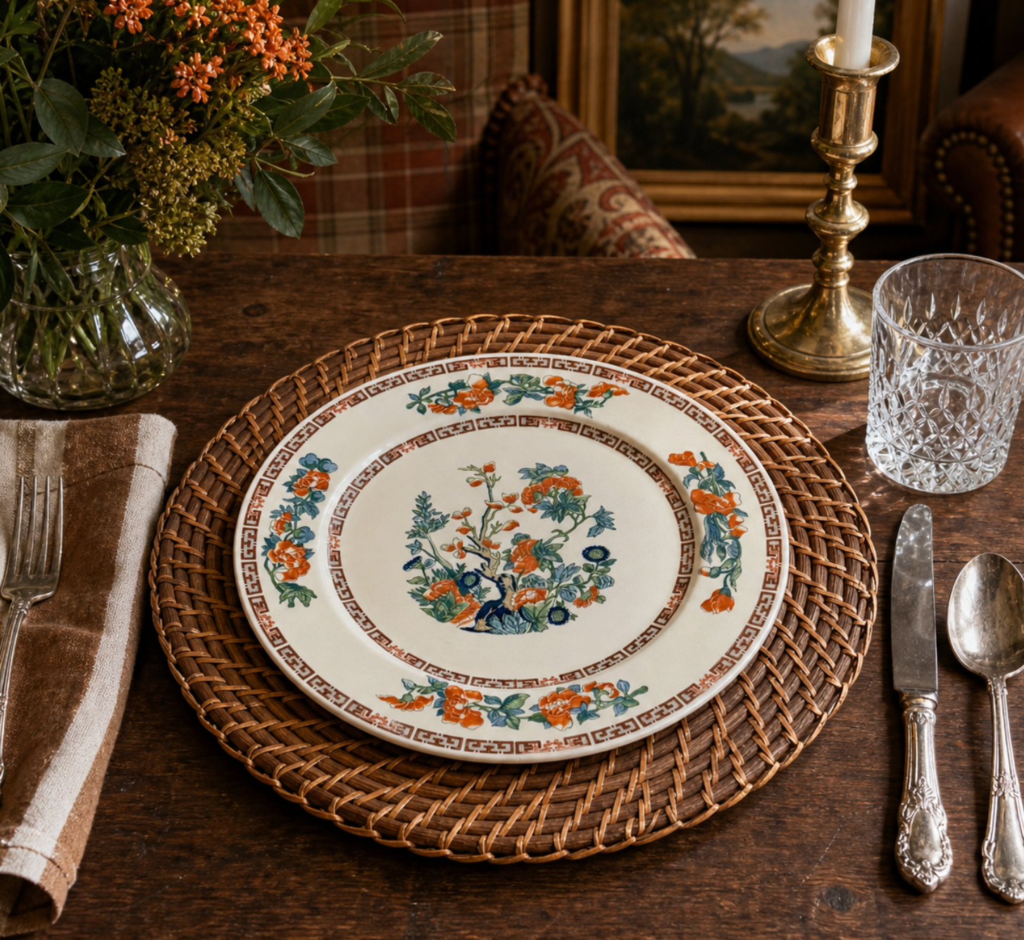 Decorative plate with floral design on a wooden table with cutlery and a vase.