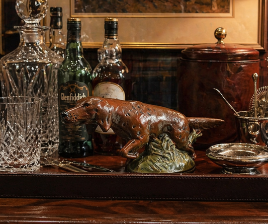 Bar setup with bottles, a glass, and a dog figurine on a wooden surface.