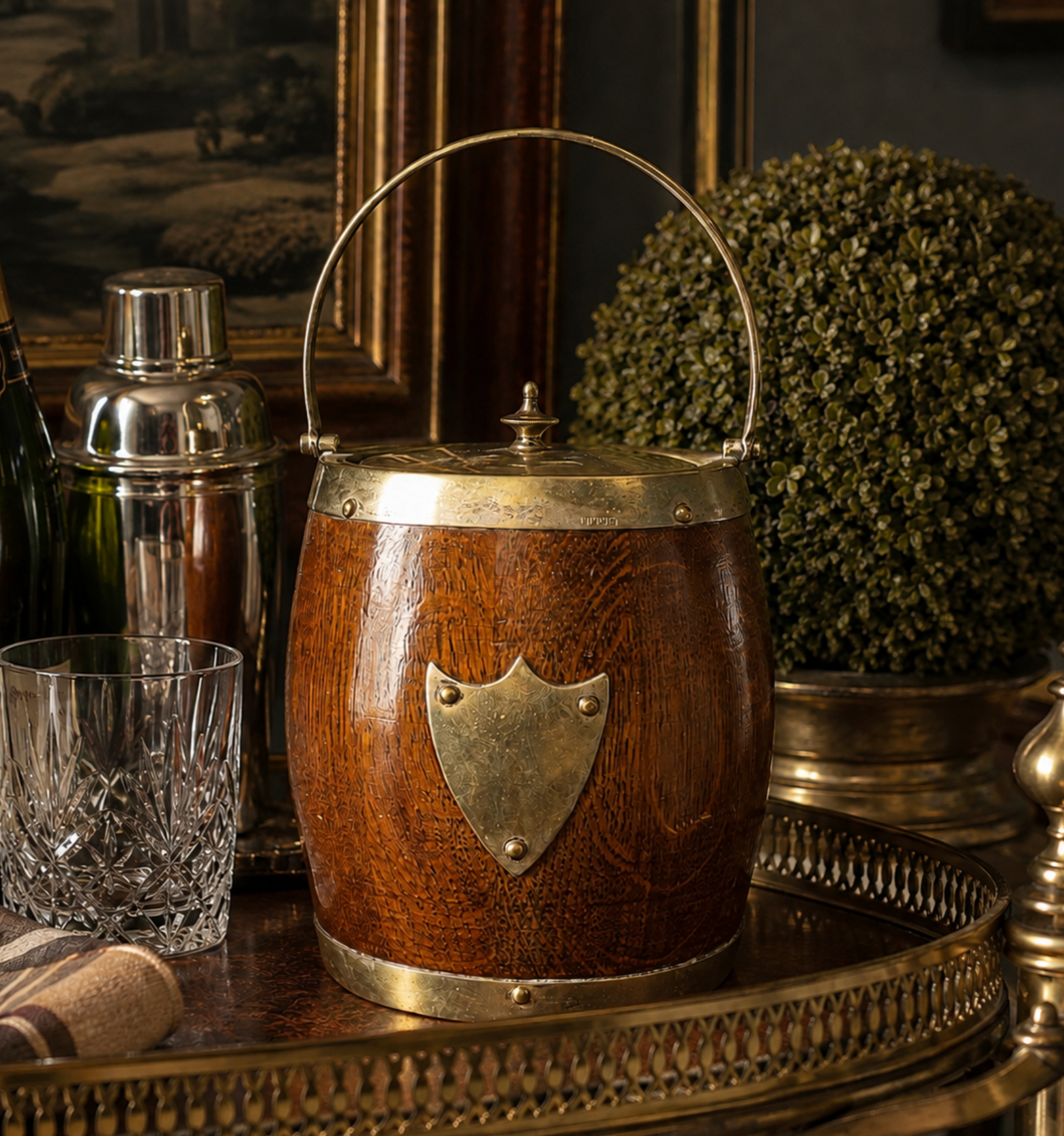 A wooden ice bucket with a brass handle and shield emblem, styled on a tray next to a crystal glass in a vintage bar setting.