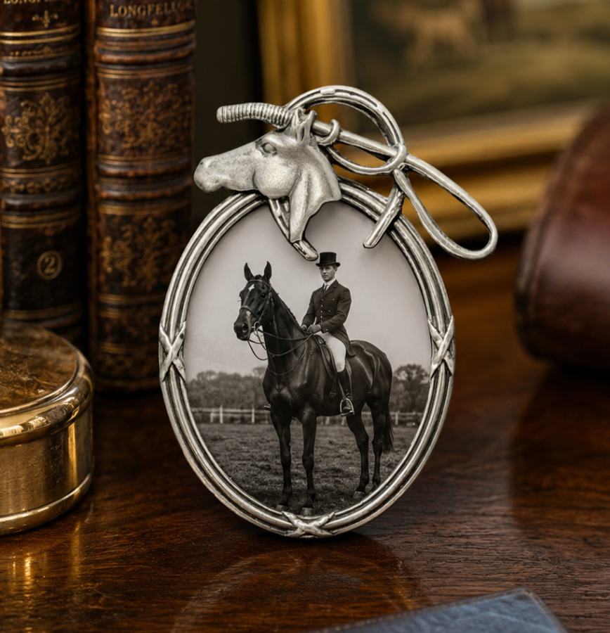 Silver keychain with a picture of a person on a horse, placed on a wooden surface with books in the background.