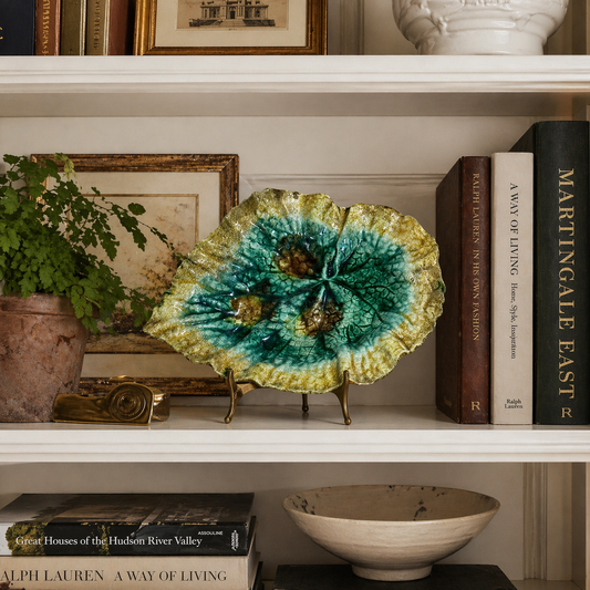 Decorative plate with green and yellow pattern on a shelf with books and a plant