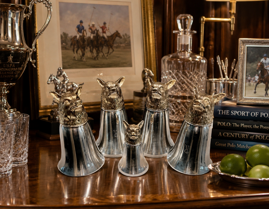 Collection of silver fox-shaped decanters on a wooden surface with polo-themed decor in the background.