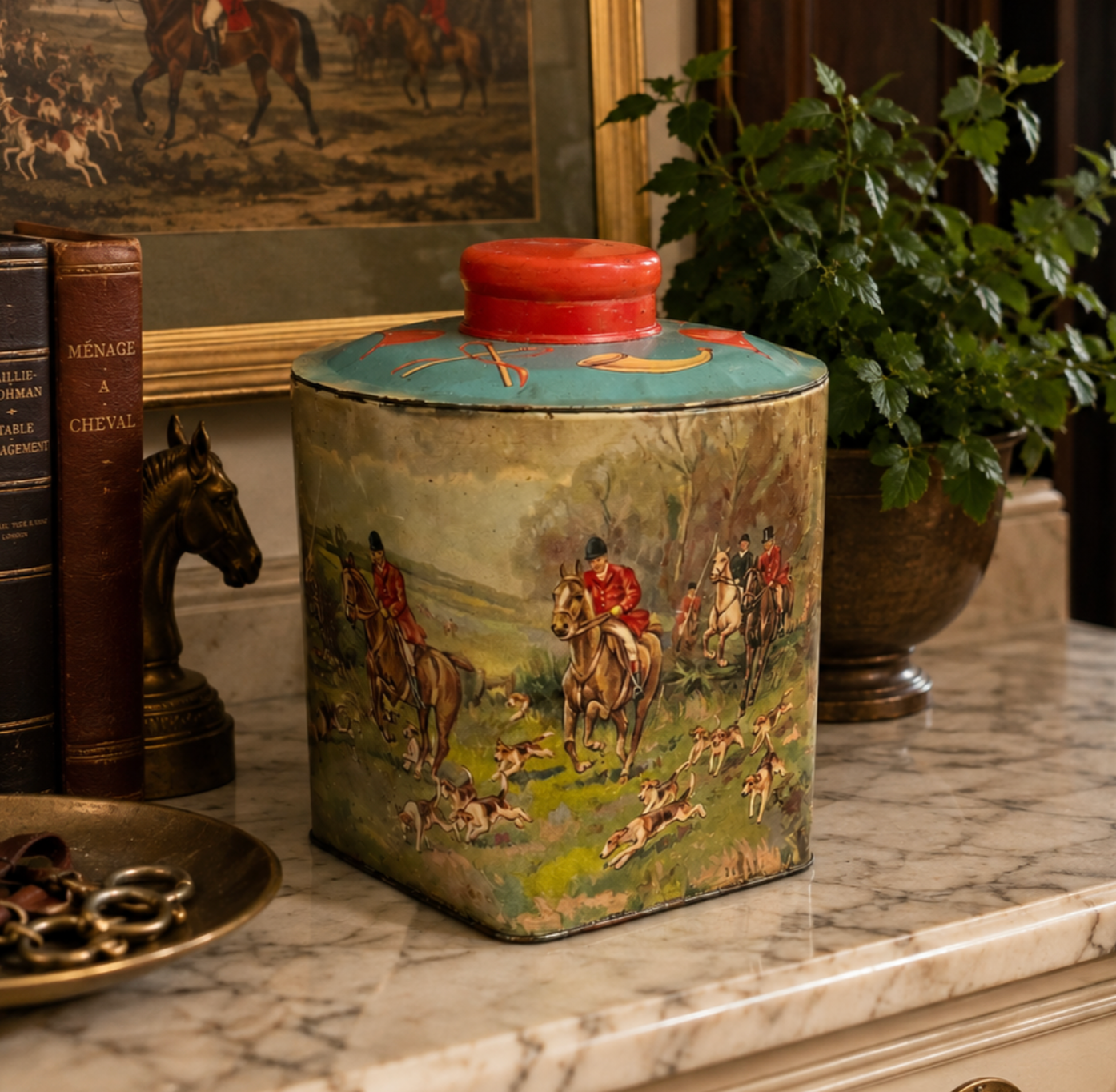 A vintage rectangular metal tea canister with a lid, decorated with a detailed hunting scene of riders on horseback and dogs, displayed on a marble countertop.