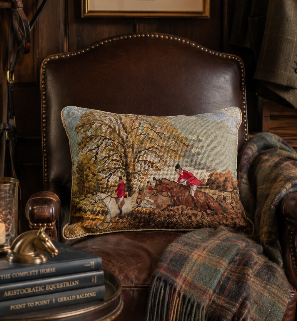 Decorative pillow with equestrian scene on a leather chair with books and a blanket.