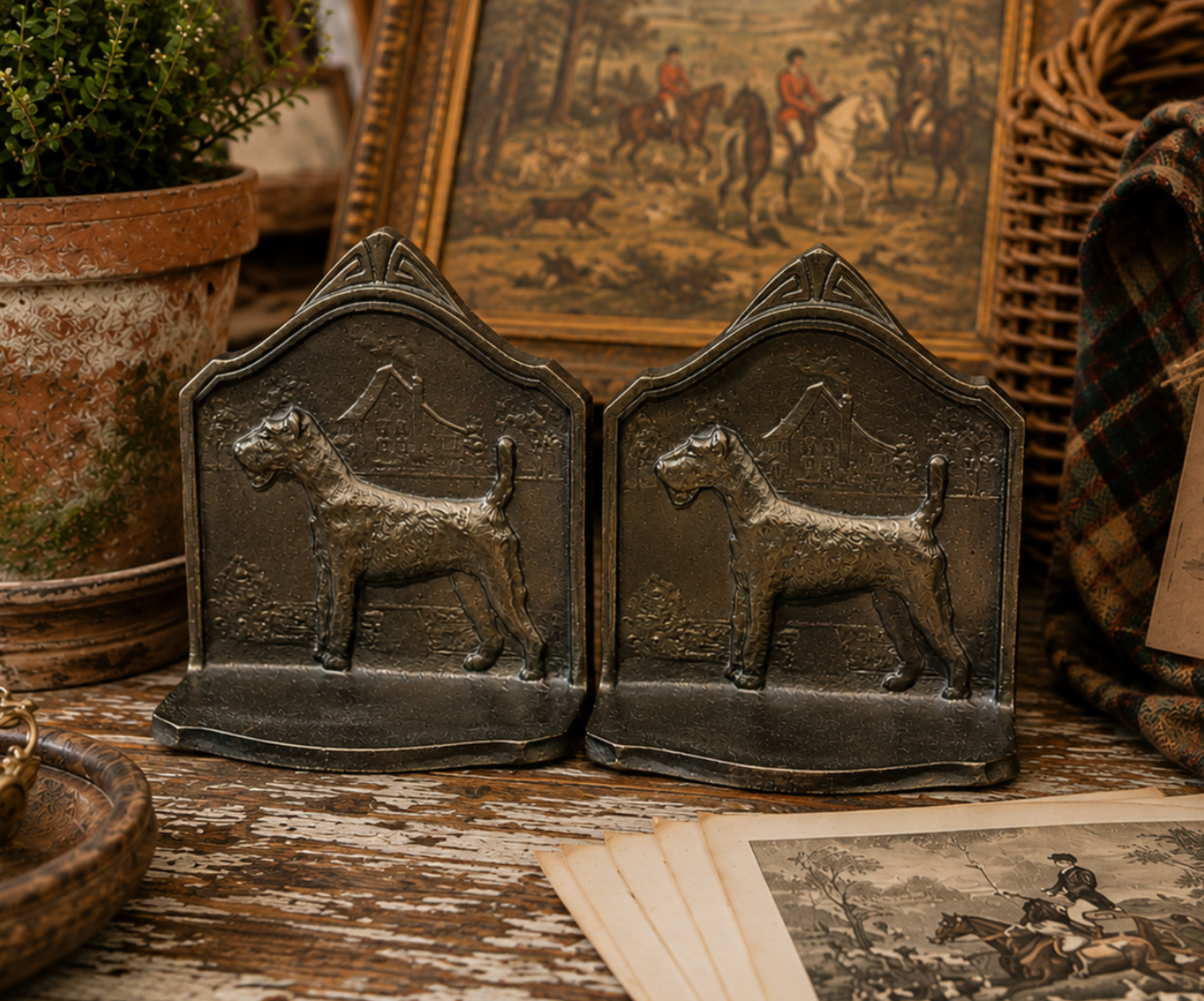 A pair of dark metal bookends shaped like Scottish Terrier dogs, displayed on a rustic wooden table with vintage-style decor in the background.