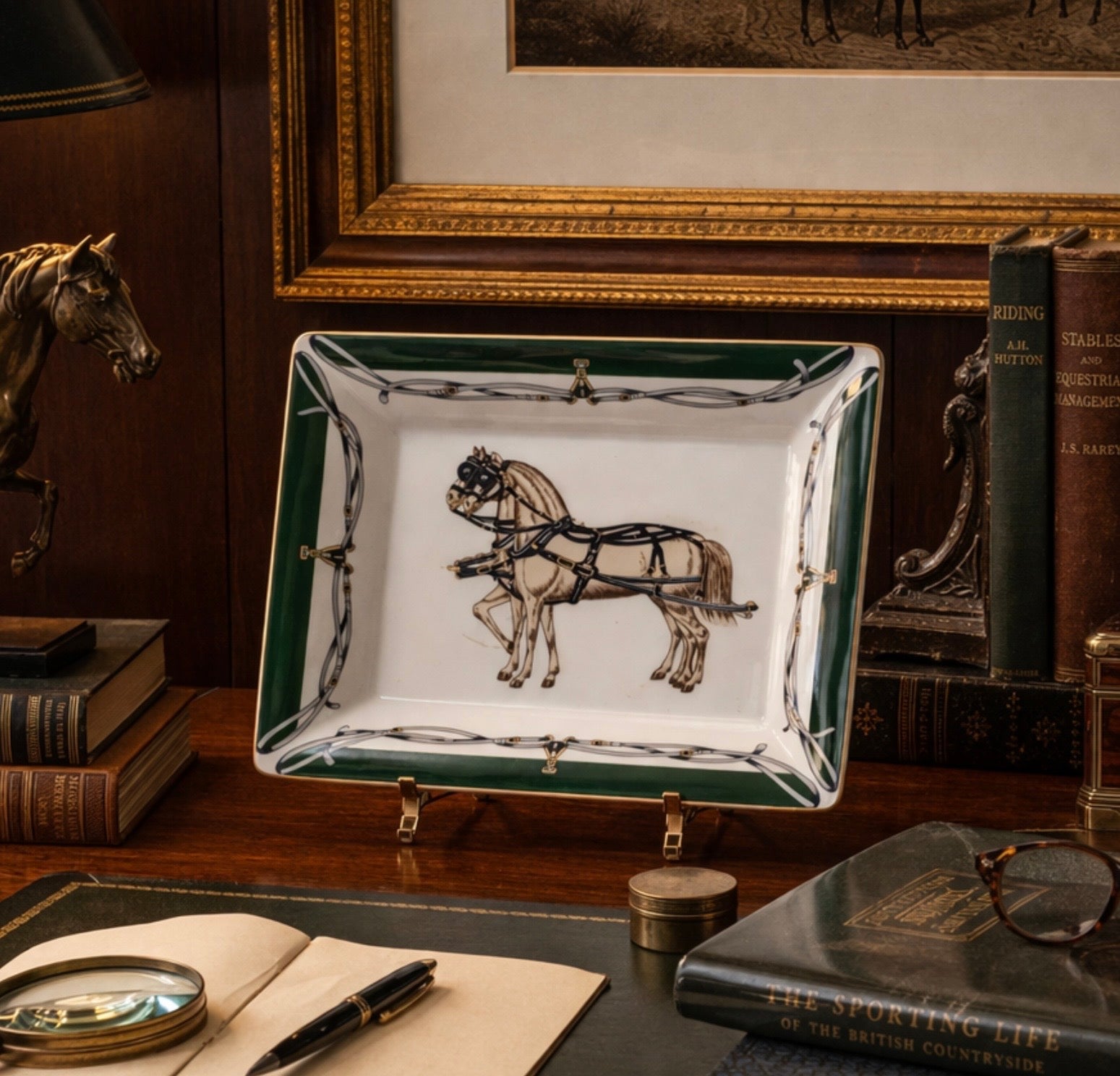 Decorative dish with horse illustration on a wooden desk with books and a magnifying glass.
