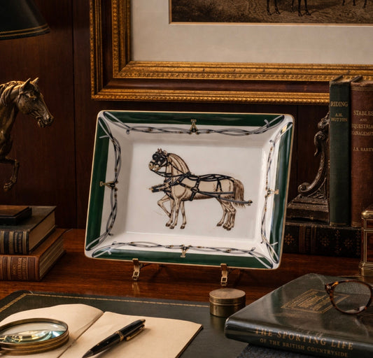 Decorative dish with horse illustration on a wooden desk with books and a magnifying glass.