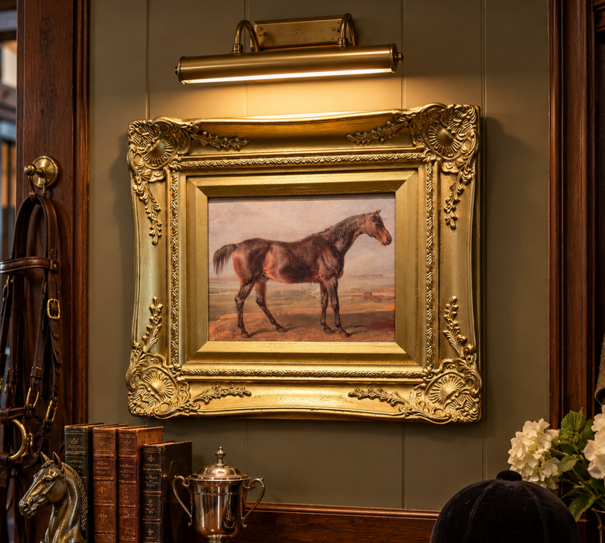 An ornate gold-framed painting of a brown horse in a landscape, displayed on a dark paneled wall under a brass light fixture in a vintage interior setting.