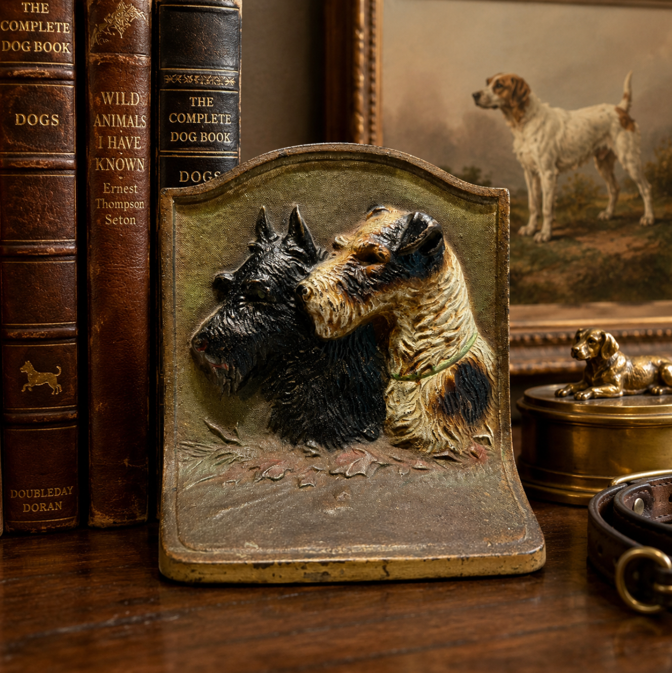 A decorative bookend featuring sculpted Scottish Terrier dogs on an aged, distressed metal plate, styled on a wooden table next to vintage dog books.