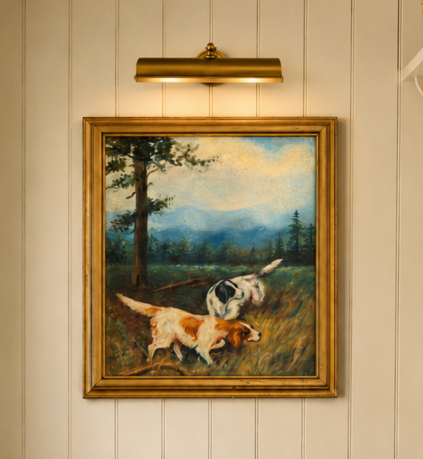 Framed painting of two dogs in a field on a wall with a light fixture above.