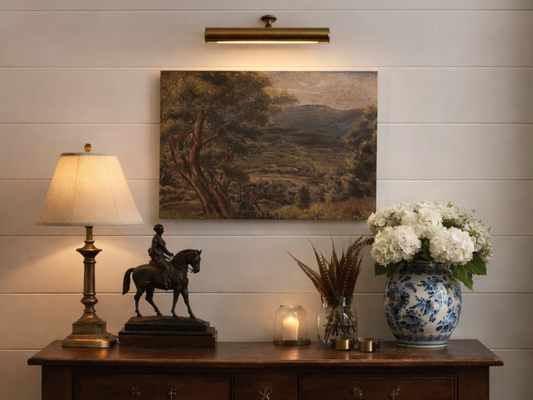 Decorative setting with a lamp, sculpture of a person on a horse, painting, and vase with flowers on a wooden surface.