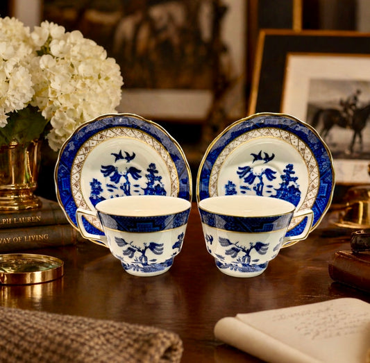 Two blue and white teacups with matching saucers on a wooden surface.