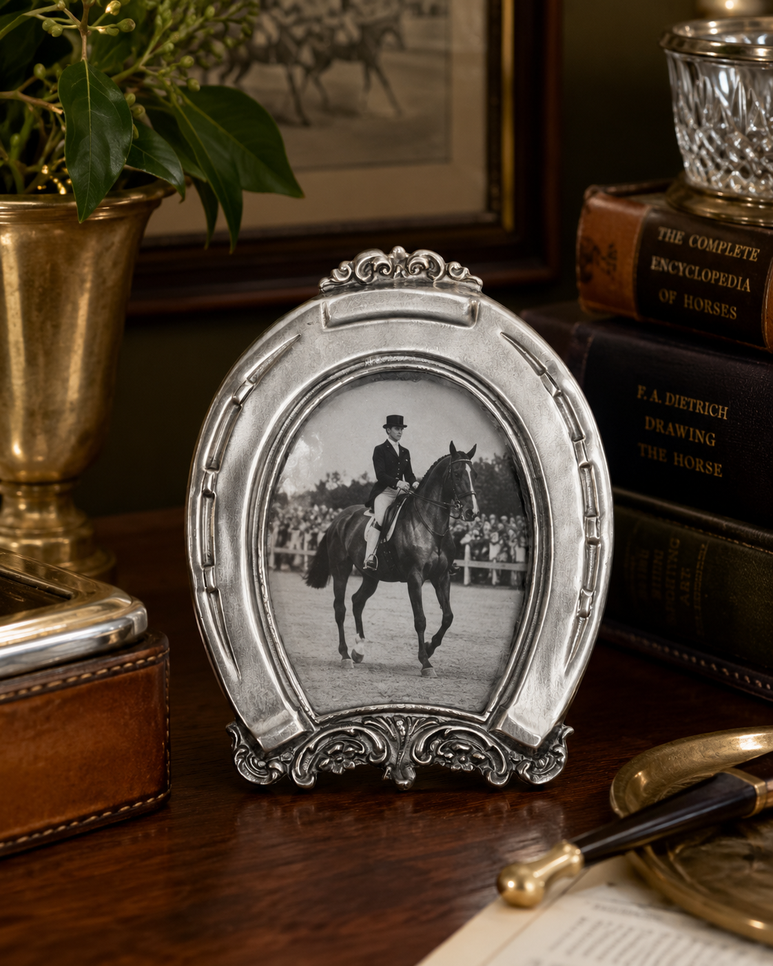Decorative frame with a photo of a person on horseback on a wooden surface with books and a plant.
