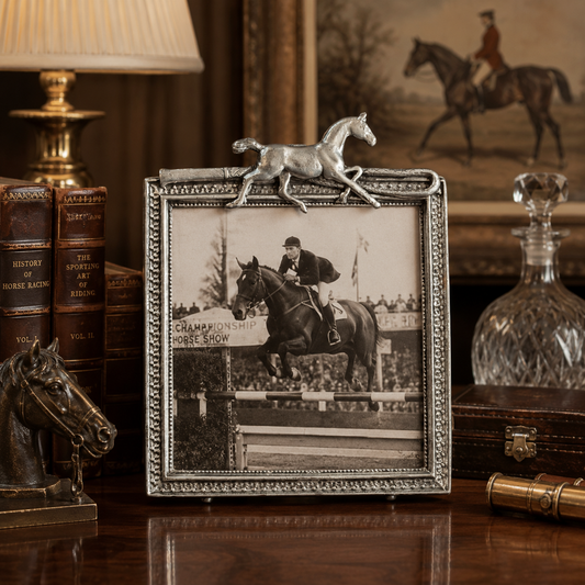 Decorative frame with a horse and rider photo on a wooden surface with books and a lamp.