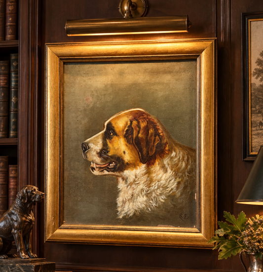 A framed oil painting of a Saint Bernard dog in profile, set in an ornate gold frame on a dark wood wall with a lamp, books, and a small dog statue nearby.