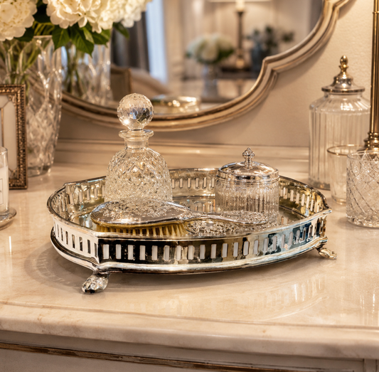 A decorative silver tray with cut-glass items and a hair brush, styled on a marble console table in an elegant interior setting with a mirror and glassware in the background.