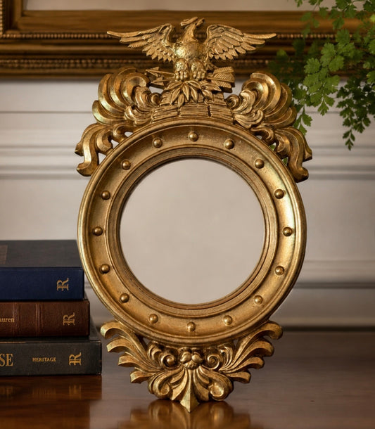 Decorative gold mirror with an eagle emblem on a surface with books in the background.