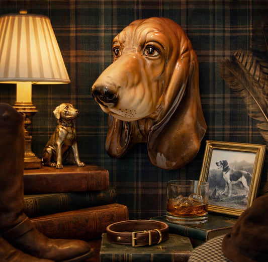 Decorative scene with a dog head sculpture, books, a lamp, and a glass of whiskey on a plaid wall background.