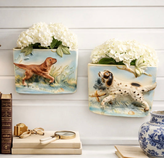 Two decorative wall plaques with dogs on a white wooden surface with books and a vase.